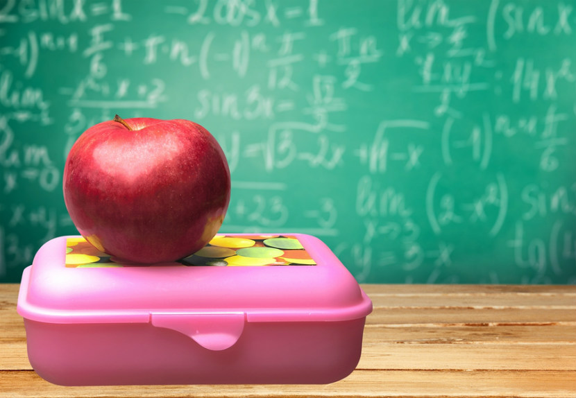 Pomme posée sur une boîte à lunch devant un tableau noir à l’école